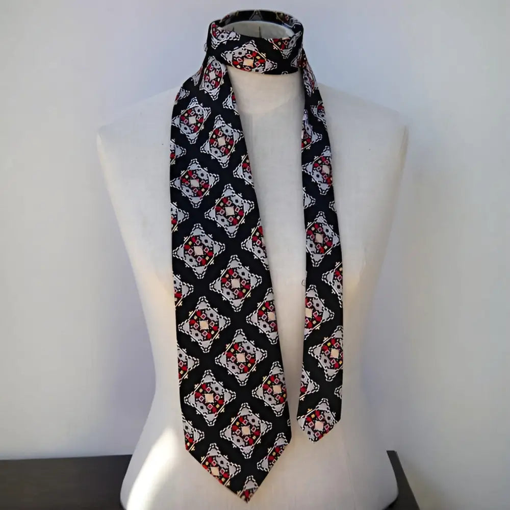 A black silk cravat with a white and red geometric pattern is elegantly displayed on a mannequin